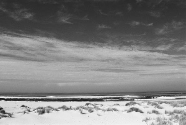 Reserva de São Jacinto, Aveiro, late 1990s. The beach stretches in quiet harmony between sand and sky. The fine texture of the dunes contrasts with the soft horizon of the sea, while the layered clouds add depth to the scene. A simple composition that captures the vast calm of this place.